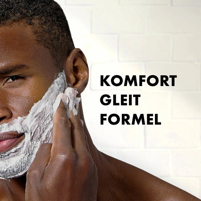 Man shaving with a close-up of his face, featuring the text 'KOMFORT GLEIT FORMEL' on a white tiled wall background.